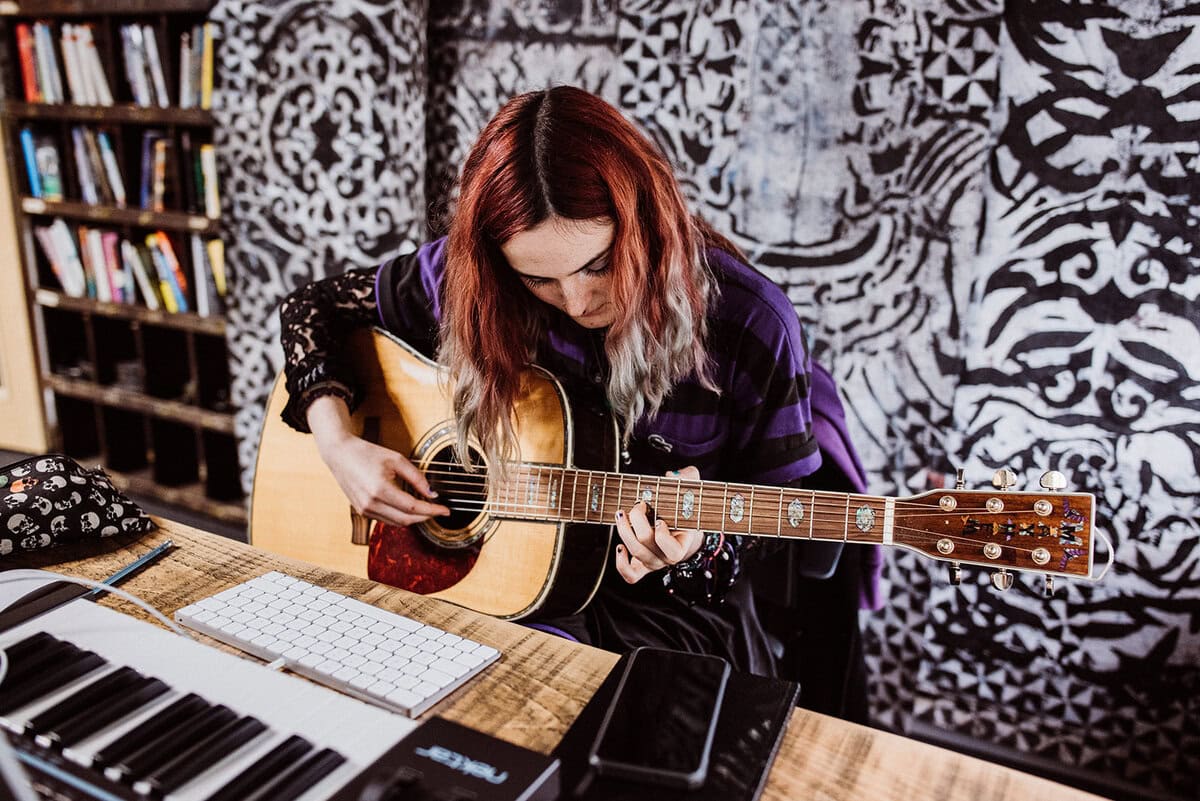 Songwriter creating a track using guitar and digital audio workstation - representing music production jobs and songwriting careers in the music industry.