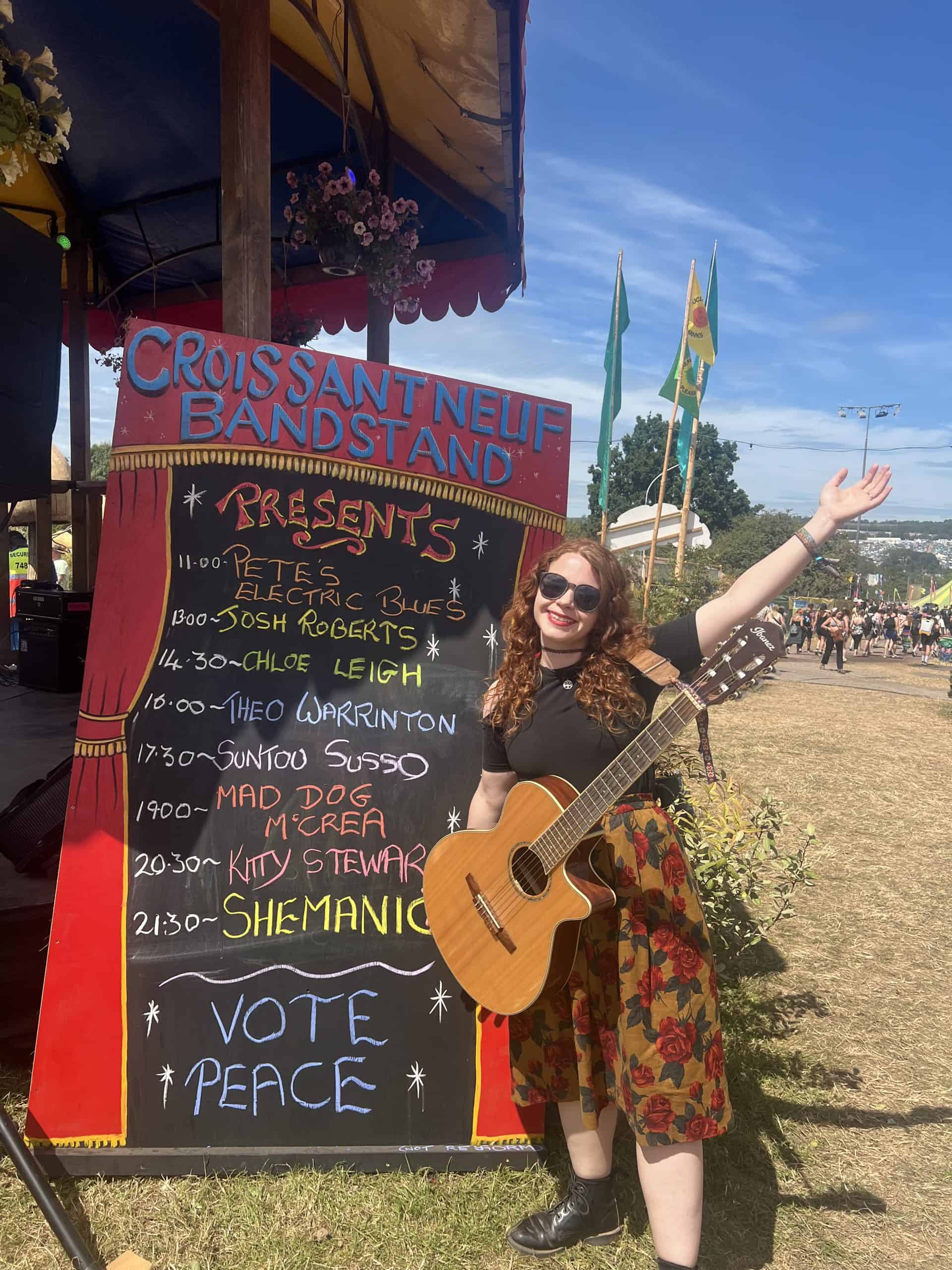Chloe Leigh next to the Glastonbury line up for the Croissant Neuf Bandstand.